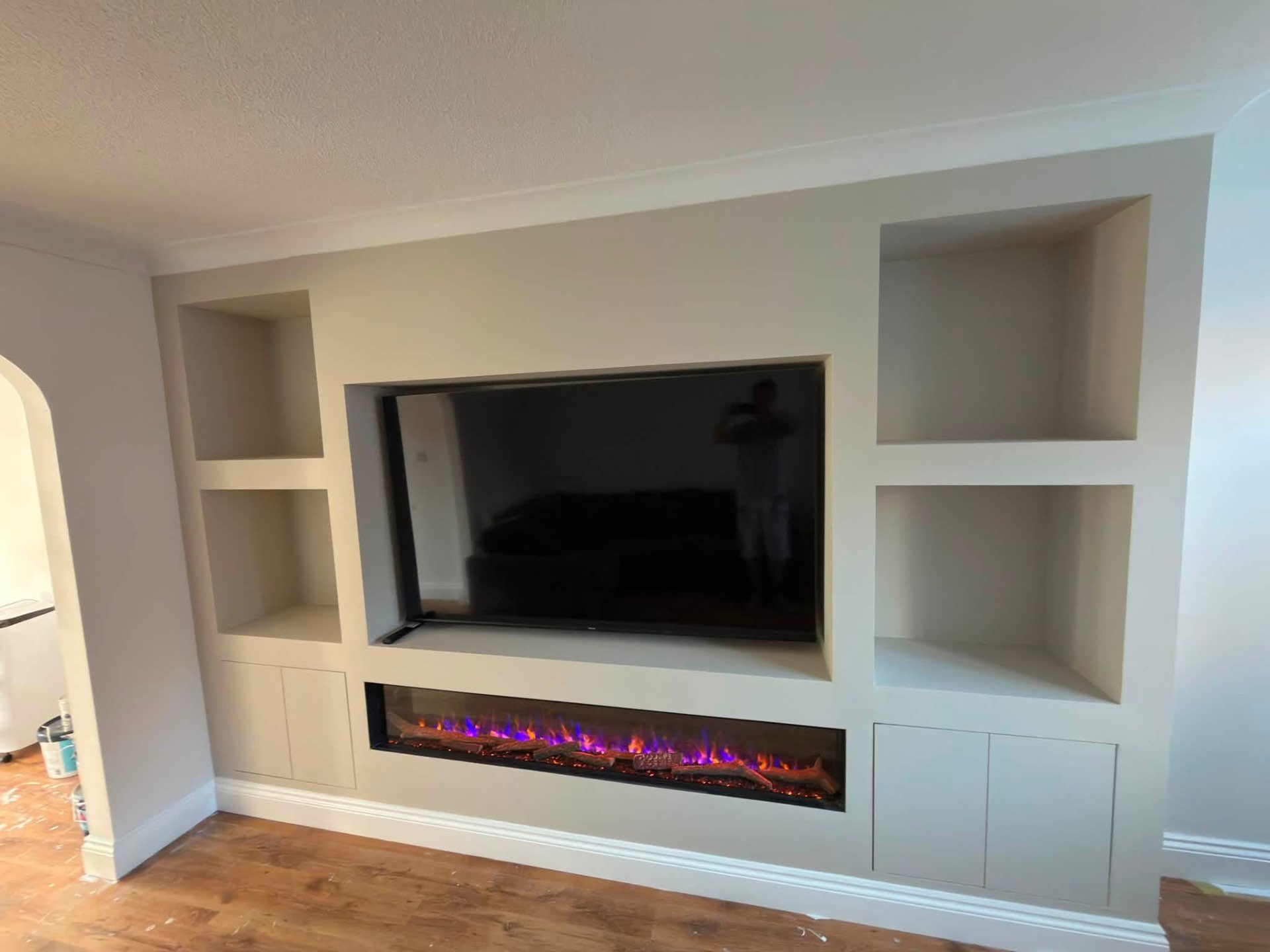 Bespoke media wall with inset fireplace and alcove shelving in a soft stone finish